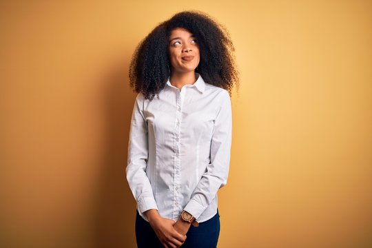 Young beautiful african american elegant woman with afro hair standing over yellow background smiling looking to the side and staring away thinking.
