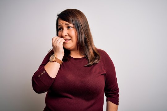 Beautiful brunette plus size woman wearing casual sweater over isolated white background looking stressed and nervous with hands on mouth biting nails. Anxiety problem.