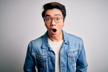 Fototapeta premium Young handsome chinese man wearing denim jacket and glasses over white background afraid and shocked with surprise expression, fear and excited face.