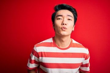Young handsome chinese man wearing casual striped t-shirt standing over red background looking at...