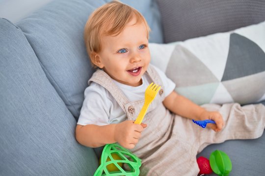 Adorable blonde toddler smiling happy sitting on the sofa playing with plastic meals toys at home