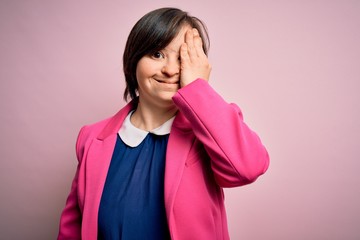 Young down syndrome business woman over pink background covering one eye with hand, confident smile...