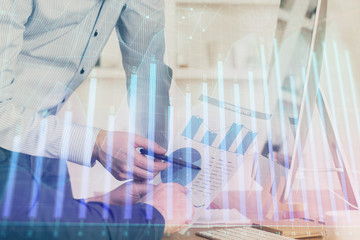 Double exposure of chart with businessman typing on computer in office on background. Concept of hard work.