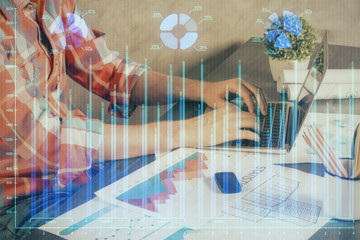 Double exposure of stock graph with businessman typing on computer in office on background. Concept of hard work.