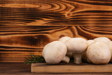 White mushrooms (champignons) and rosemary leaves on wooden table with copy space