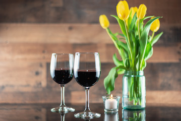 Two glasses of red wine with flowers and a candle