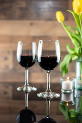 Two glasses of red wine on a table with candles and flowers
