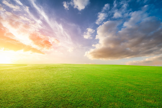 Green grass field and colorful sky clouds at sunset.