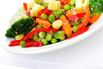Colorful mix of cut fresh variety vegetables for vegetarian diet-carrots, tomatoes, corn, peas, sweet peppers, broccoli in white dish on white background. Concept of healthy eating. Tilt frame on left
