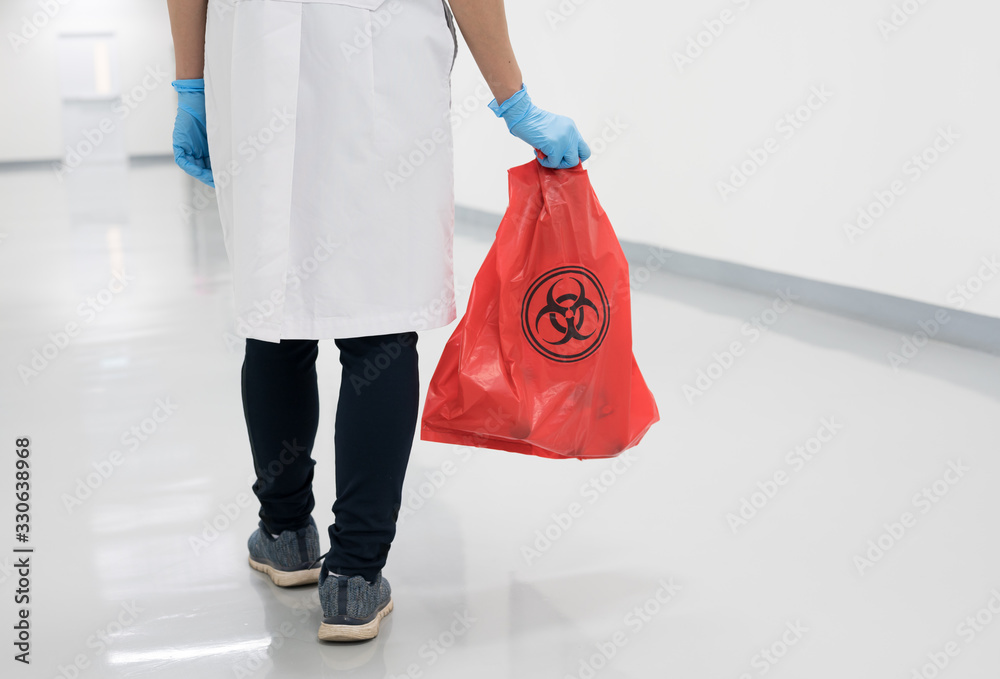 Wall mural scientist wearing blue gloves and red bag with bioharzard sign.a woman worker hand holding red garba