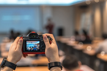 Closeup photographer hand taking photo of Asian speaker on the stage when presenting the knowledge over Rear view of Audience listening in the study room, seminar business and education concept