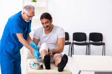 Leg injured man visiting old doctor in first aid concept