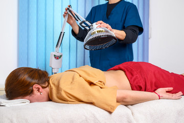 Therapist doing healing infrared treatment on woman back . Alternative medicine, physiotherapy,...