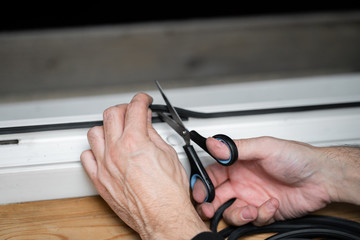 Professional window repair and installation technician, cuts sealing rubber for installation in a pvc window