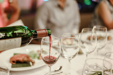 Waitress is pouring red wine in glasses for wine tasting event on the table in restaurant . Blurred background. wine, tasting, pour, bartender, beverage, dinner concept.
