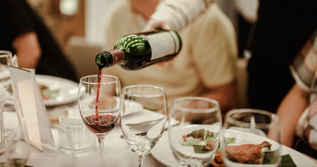 Waitress is pouring red wine in glasses for wine tasting event on the table in restaurant . Blurred background. wine, tasting, pour, bartender, beverage, dinner concept.