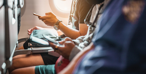 The tourists who are playing the phone and have a ticket on hand on the plane that is preparing to take-off. Airplane, Travel, Smartphone, Airport, ticket, technology concept.