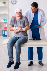 Young male doctor and old patient in first aid concept