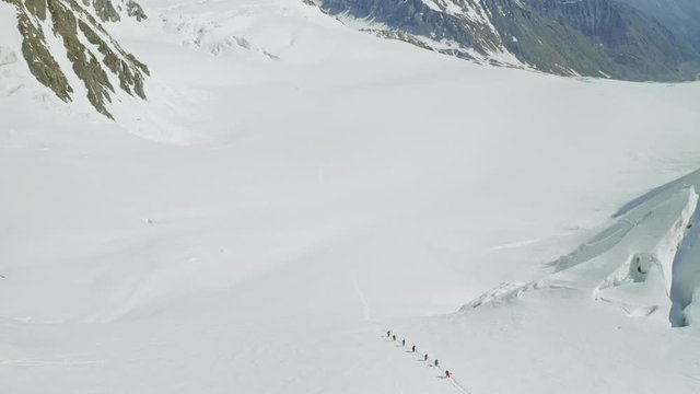 Aerial fly above tourists climbs up on spacious snow slope, mountain expedition