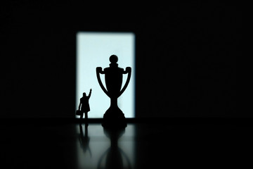 Obraz premium Business strategy conceptual photo - Silhouette of miniature businessman pointing on winning trophy in the podium