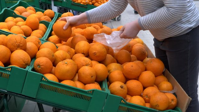 close-up hands of adult woman picking orange in supermarket and puts fruits on knitted mesh made of eco-friendly materials. selective focus