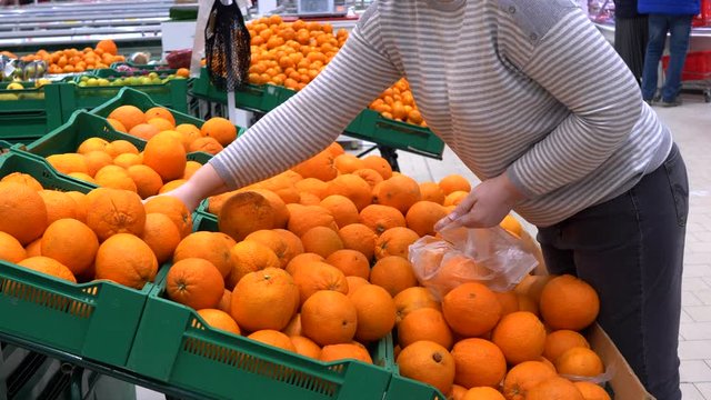 close-up hands of adult woman picking orange in supermarket and puts fruits on knitted mesh made of eco-friendly materials. selective focus