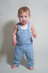  emotional portrait of a one-year-old baby in denim overalls on a uniform light background