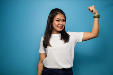 Portrait of Young beautiful asian women using white T-shirt with blue isolated background, raises arms and shows biceps