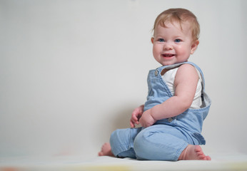  emotional portrait of a one-year-old baby in denim overalls on a uniform light background
