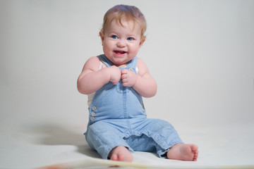  emotional portrait of a one-year-old baby in denim overalls on a uniform light background