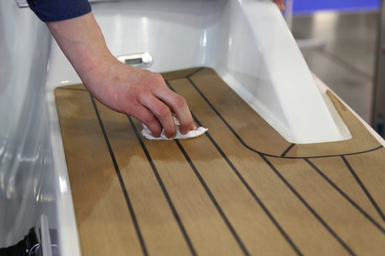 A man's hand rubs oil on marine teak on the deck of a white motor yacht , motor boat maintenance