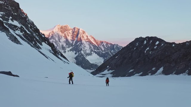 Tourists moves up over wide snow slope, alpine mountain trekking at morning dawn
