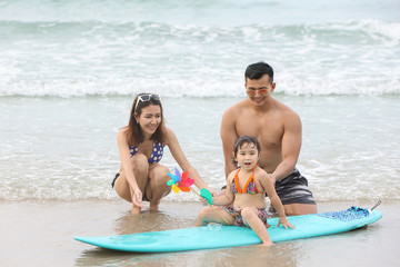 Obraz premium Young asian family and daughters who wearing swimwear are playing sand on the beach during happy and loving times with smiling face on holiday vacation.
