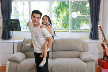Obraz premium Single parent happy family portrait. Asian father holding his daughter while he standing in living room. Single dad having a good time and his little girl is laughing. Happy family concept.