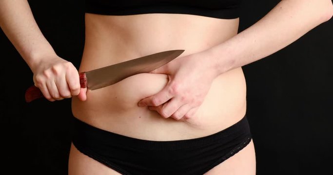 The concept of getting rid of excess weight. Girl cuts off fat deposits with belly knife/
