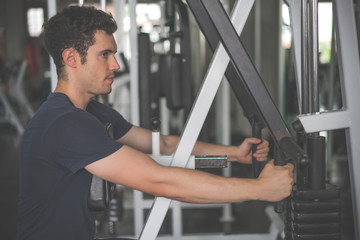 Fototapeta na wymiar Handsome man lowering weight of fitness machine and working out in the fitness gym
