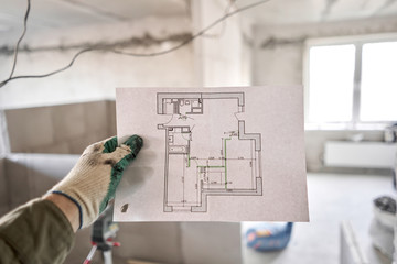 The construction worker hold in hands Architectural blueprints. Repair or construction of a new apartment. Concept for new house design or home improvement. Development of the apartment project.