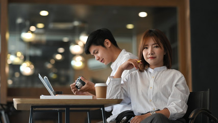 Photo of young couple working as graphic designer sitting together at wooden working table in comfortable and luxury office with blurred background.