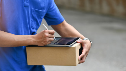 Cropped image of delivery man using a stylus pen and computer tablet for checking address of parcel...