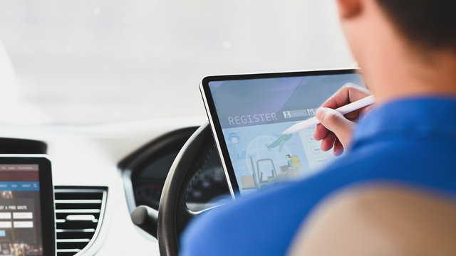 Cropped image of delivery man using a stylus pen and computer tablet for checking address of parcel location while sitting behind steering wheel in the modern van.