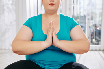 Fototapeta na wymiar Cropped image of meditating overweight young woman keeping hands in namaste gesture