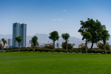 Fototapeta na wymiar Ras al Khaimah, United Arab Emirates Corniche with green grass picnic and family area, looking towards the mountains on a sunny day.