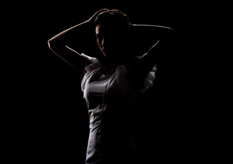 Fototapeta na wymiar Silhouette of a beautiful slender girl in a white dress on a black background