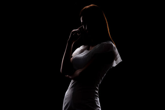 Silhouette of a beautiful slender girl in a white dress on a black background