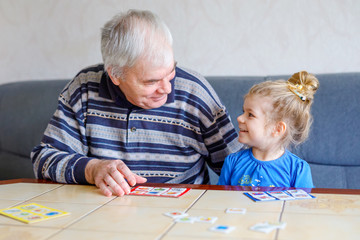 Beautiful toddler girl and grandfather playing together pictures lotto table cards game at home....