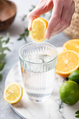 Lemon citrus water in glass. Woman hand squeeze lemon in glass of fresh clean water. Refreshing cold summer drink Lemonade © Vladislav Noseek