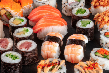 Large sushi set, close-up on a black background. An assortment of various maki, nigiri and rolls