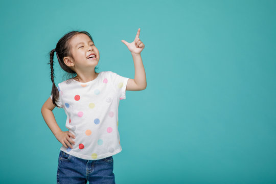 Beautiful smiling Asian little girl pointing hand to blank speech bubble, empty space in studio shot isolated on colorful blue background, Educational concept for school