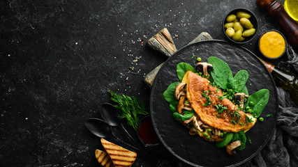 Omelet with mushrooms and spinach in a black plate. Top view. Free space for your text.