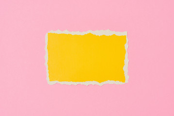 Ripped yellow paper torn edge sheet on a pink background. Template with piece of color paper